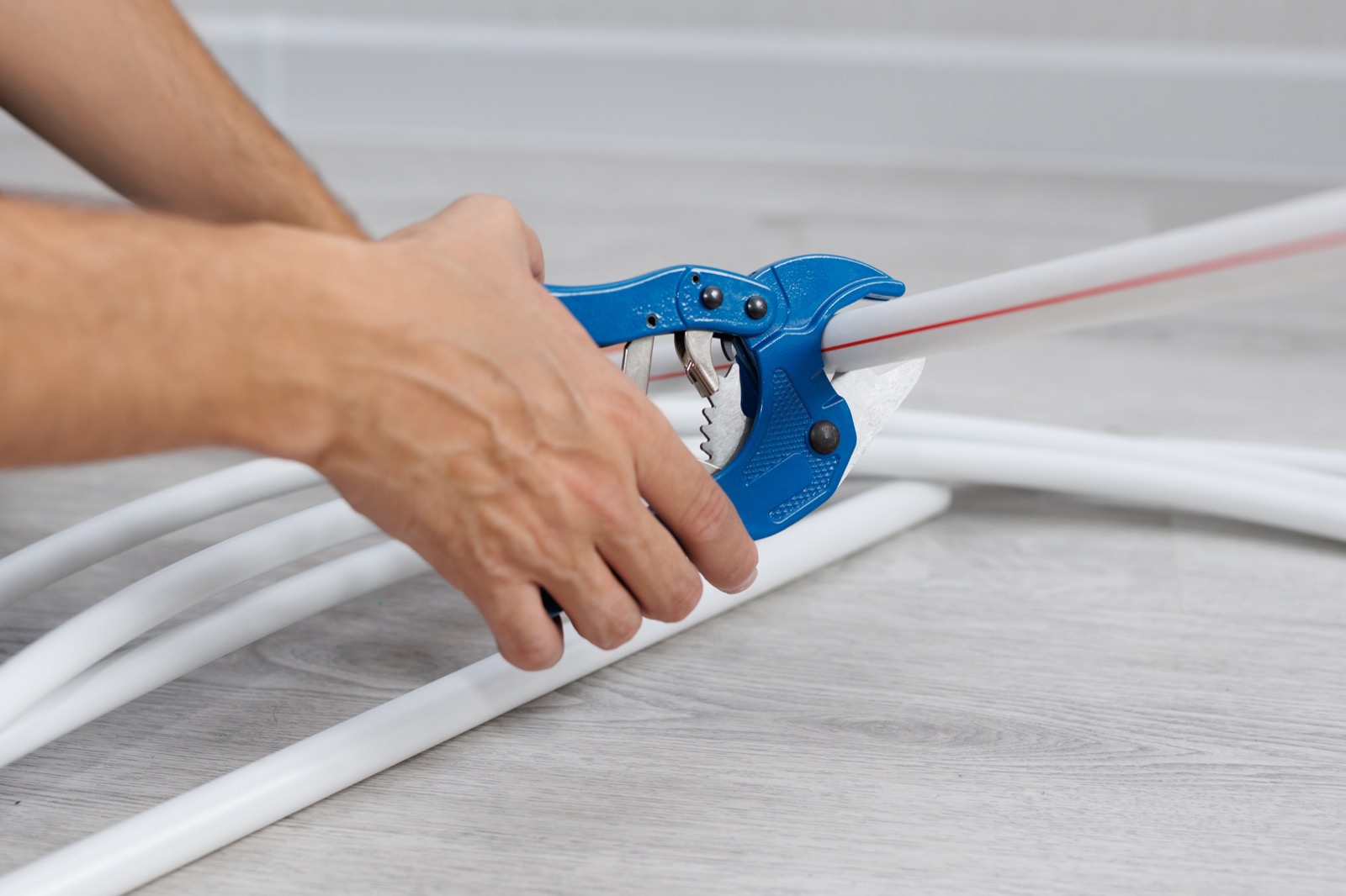 Plumber cutting PEX water line pipe with a pipe cutter