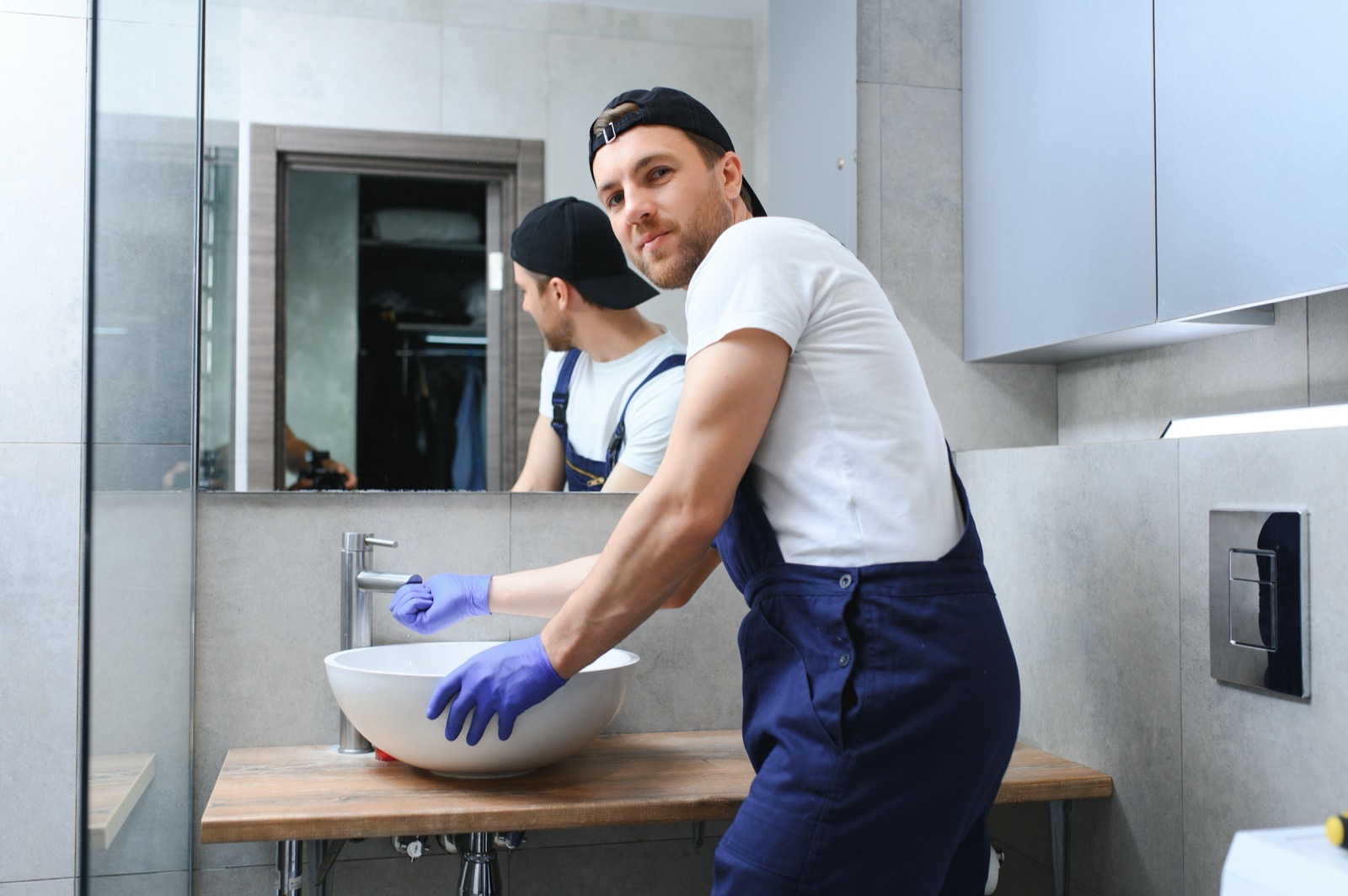 Plumber in blue gloves working in a home bathroom