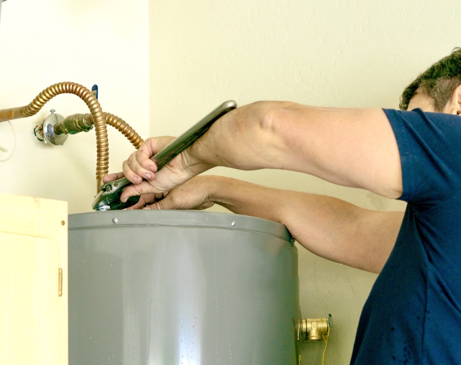 Plumber repairing a leaking water heater with a wrench
