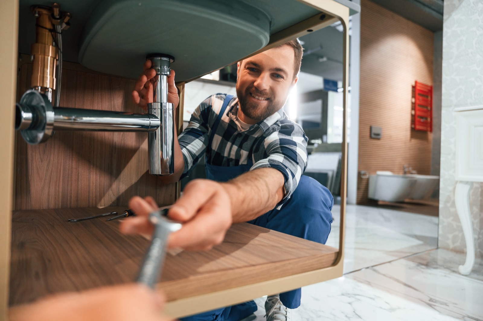 Plumber repairing supply pipes under a kitchen sink in a Hurst home