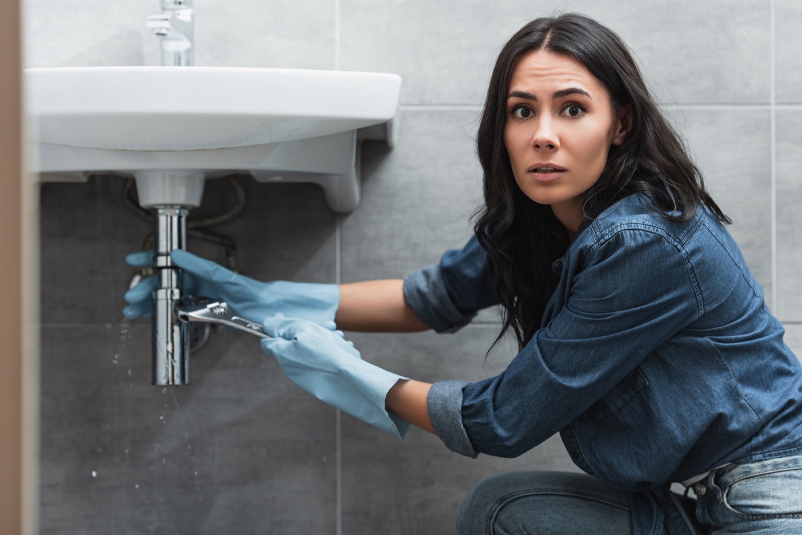 Homeowner dealing with an urgent plumbing problem in a tiled bathroom